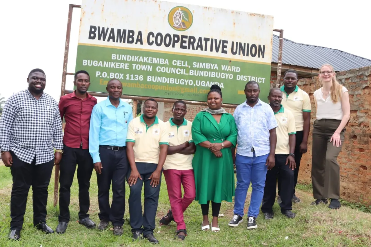 The Bwamba Cooperative Union team and a visiting partner standing together in front of the union's signboard